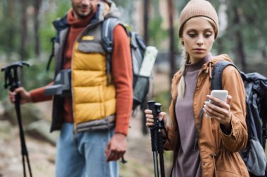 woman holding smartphone while searching location near blurred boyfriend