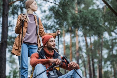 couple with hiking sticks resting after trekking in forest 