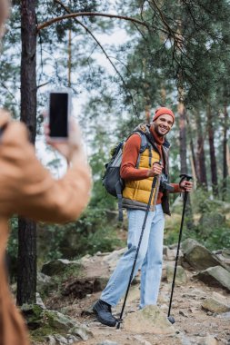 blurred woman taking photo of smiling boyfriend on smartphone with blank screen 
