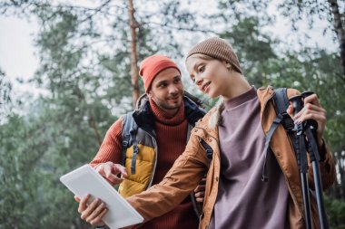 man looking at girlfriend and pointing at digital tablet in forest 