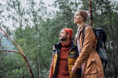 young and cheerful couple holding hands in forest 