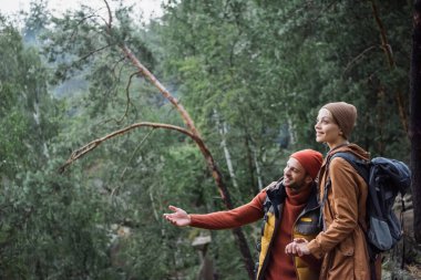 man pointing with hand while holding hands with cheerful girlfriend in forest 