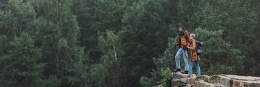 couple with hiking sticks standing on rocky cliff, banner