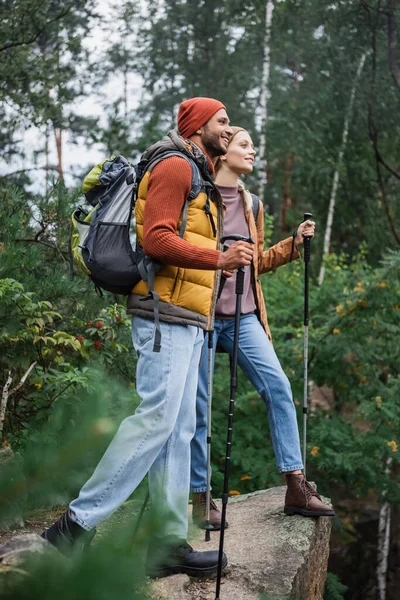 森の中で彼氏の近くを歩くハイキング棒を持つ幸せな女性の完全な長さ — ストック写真