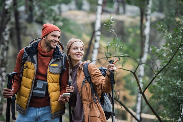 happy woman pointing with finger near cheerful boyfriend with smartphone 