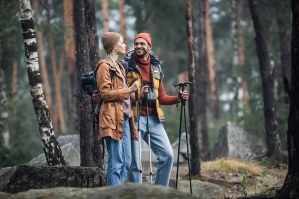 Cheerful Couple Hats Holding Hiking Sticks While Hugging Forest — Stockfoto