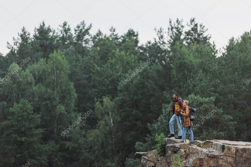 couple with hiking sticks standing on rocky cliff 