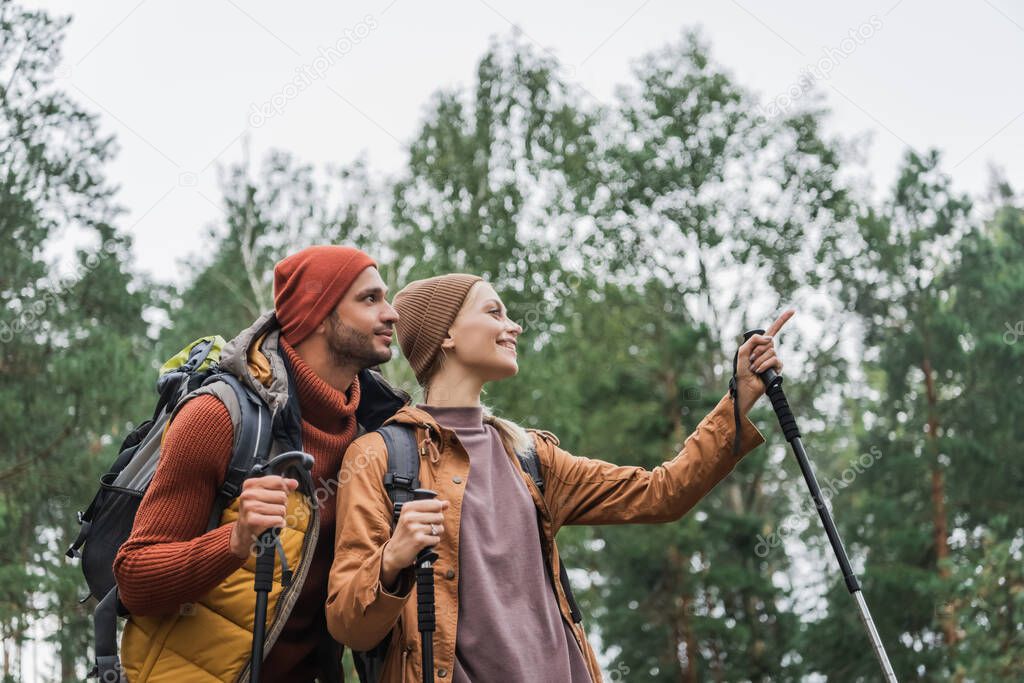 happy young woman pointing away with finger near boyfriend in forest 