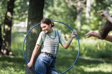 Smiling teenager holding hula hoop in park  clipart