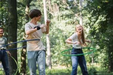 Parktaki bulanık arkadaşlarının yanında hula hoop çeviren pozitif genç. 
