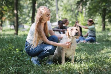 Gülümseyen genç av köpeği parkta bulanık arkadaşlarının yanında. 