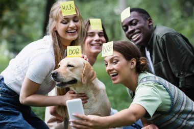 Parkta Retriever 'ın yanında oynarken selfie çeken pozitif etnik gençler. 