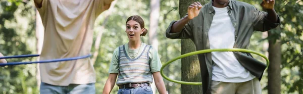 兴奋的少女看着镜头旁边的跨种族朋友与呼啦圈在公园 — 图库照片