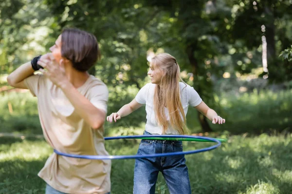 Oldalnézet Mosolygós Lány Csavaró Hullahopp Karika Közelében Elmosódott Barát Parkban — Stock Fotó