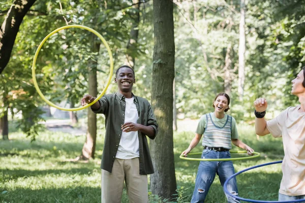 Usmívající Africký Americký Teenager Drží Hula Obruč Blízkosti Přátel Parku — Stock fotografie