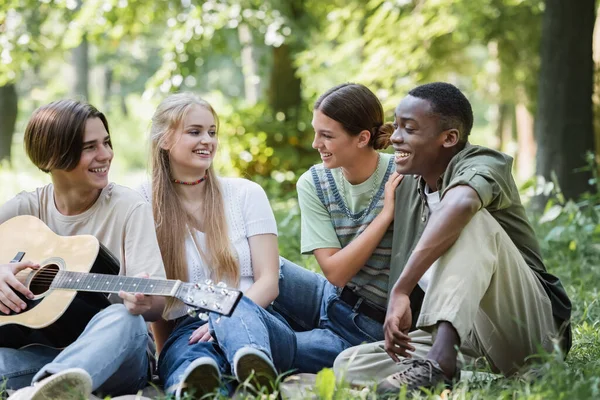 Usmívající Teenageři Hrající Akustickou Kytaru Blízkosti Mezirasových Přátel Trávě — Stock fotografie