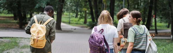 Adolescentes Interraciales Con Mochilas Monopatín Caminando Parque Pancarta —  Fotos de Stock