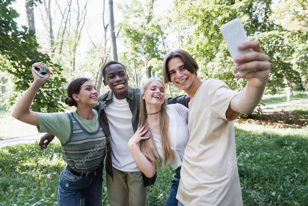 Smiling teenager taking selfie with interracial friends in park 