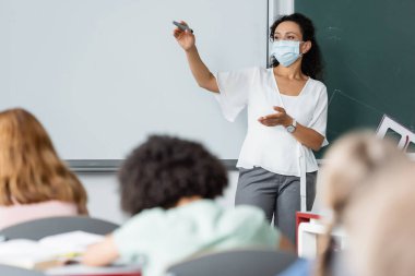 african american woman pointing with hand near whiteboard and blurred schoolkids clipart