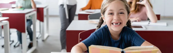 Opgewonden Schoolmeisje Met Boek Glimlachen Camera Buurt Wazig Klasgenoten Leraar — Stockfoto