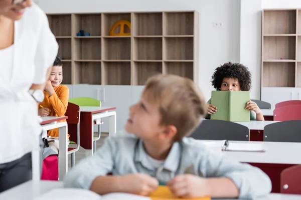 African American Schoolboy Holding Book Blurred Classmates Teacher — Stock Photo, Image