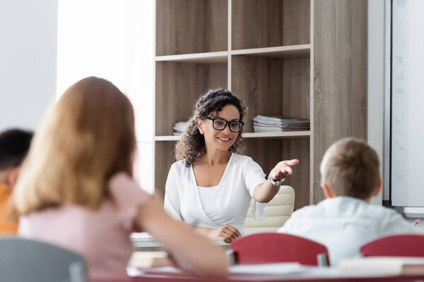 positive african american teacher pointing with hand near blurred pupils