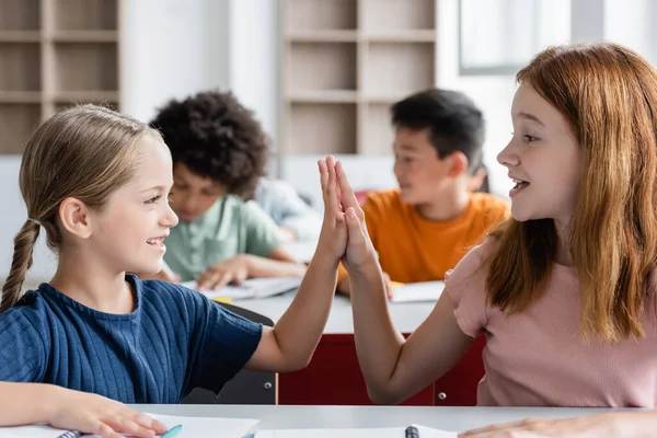 Feliz Colegialas Dando Alta Cinco Durante Lección Cerca Borrosa Interracial —  Fotos de Stock