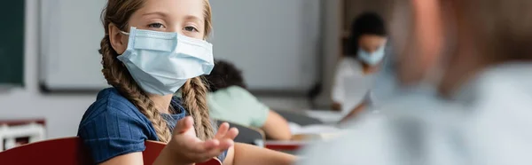 Schulmädchen Medizinischer Maske Zeigt Mit Der Hand Auf Verschwommenen Schüler — Stockfoto