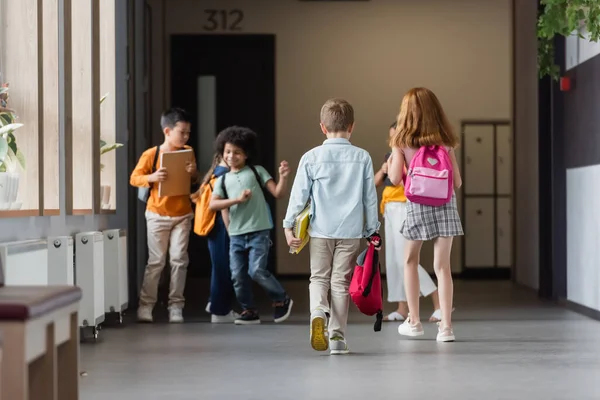 学校の廊下にはバックパックやノートがある多民族の子供たち — ストック写真