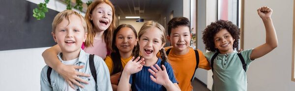 overjoyed multiethnic classmates waving hands and showing rejoice gesture in school hall, banner
