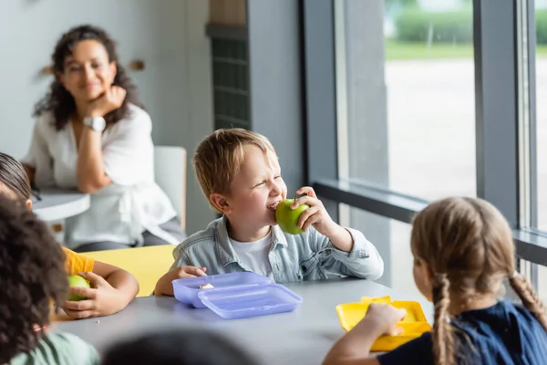 Boy Eating Apple Classmates Blurred African American Teacher — Stock Photo, Image