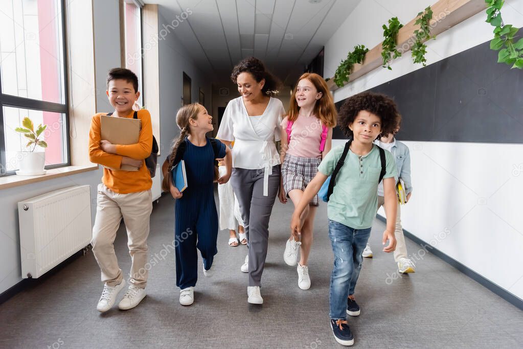 happy multiethnic kids and african american teacher walking in school corridor