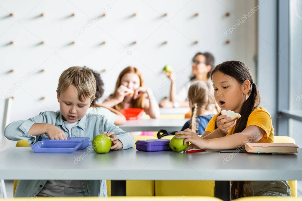 asian schoolgirl eating sandwich near classmates during lunch break