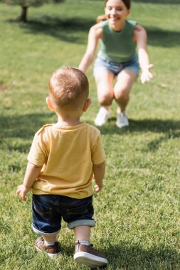 Bulanık, neşeli annesinin yanında uzanmış elleri olan küçük bir çocuğun arka görüntüsü.