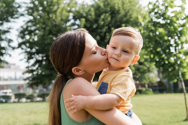 若い母親が腕を握って幼い息子にキスをし — ストック写真