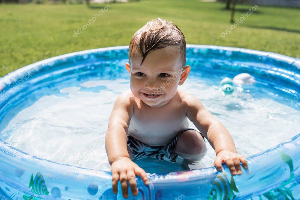 smiling toddler boy sitting in inflatable pool 