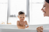boldog kisgyerek kezében zuhanyfej közelében elmosódott és vidám anya előtérben 