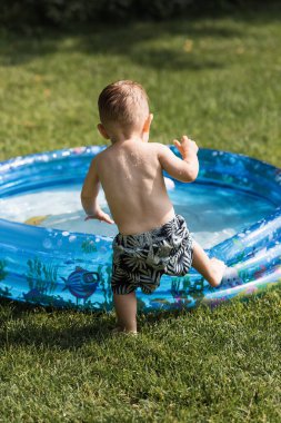 Yüzme şortlu, şişme havuzun yanındaki küçük çocuğun arka görüntüsü.