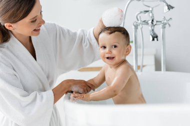 Bornozlu neşeli anne banyo yapan mutlu çocuk küvette yatıyor. 