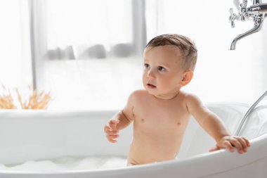 Çıplak çocuk küvette banyo yapıyor. 