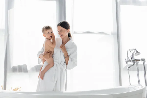 Cheerful Mother Bathrobe Holding Arms Naked Toddler Son Bathtub — Stock Photo, Image