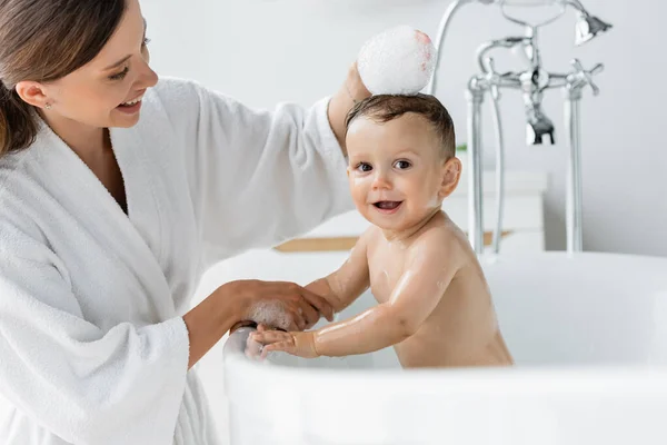 快乐的母亲穿着浴衣洗澡快乐的幼儿在浴缸里洗澡 — 图库照片