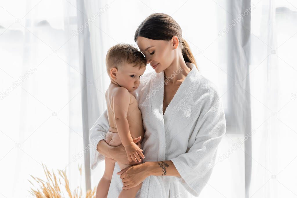 caring mother in bathrobe holding in arms naked toddler son 