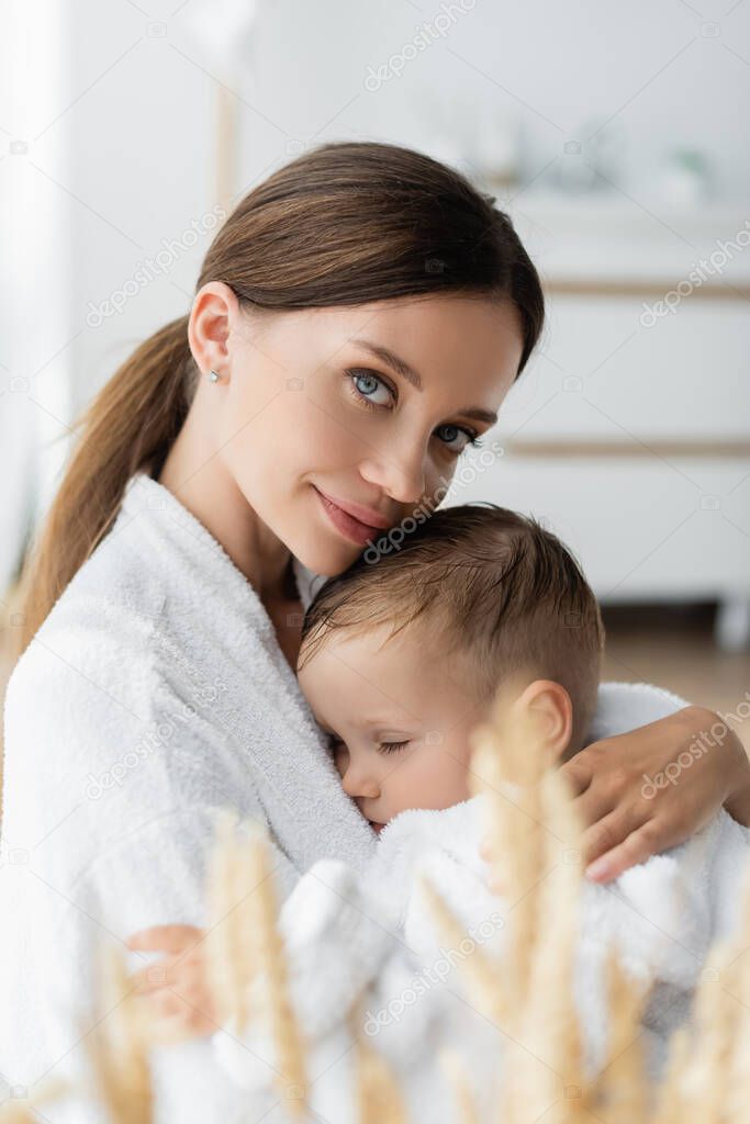 young mother hugging toddler son in bathrobe