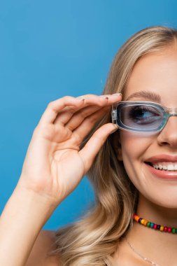 Mavi üzerine izole edilmiş güneş gözlüğü takan neşeli kadın manzarası.