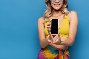 Sarı bikinili mutlu genç bir kadın elinde akıllı telefonla mavi ekranda izole edilmiş beyaz bir ekran tutuyor.