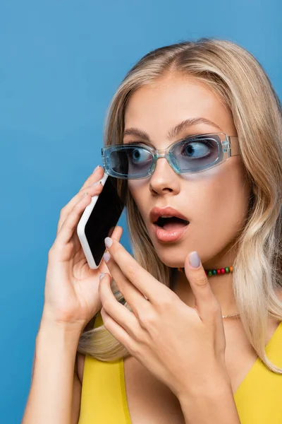 Geschokt Jonge Vrouw Zonnebril Praten Smartphone Geïsoleerd Blauw — Stockfoto