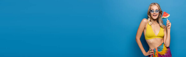 молодая женщина в желтом бикини топ с палочкой эскимо с арбузом на синем, баннер