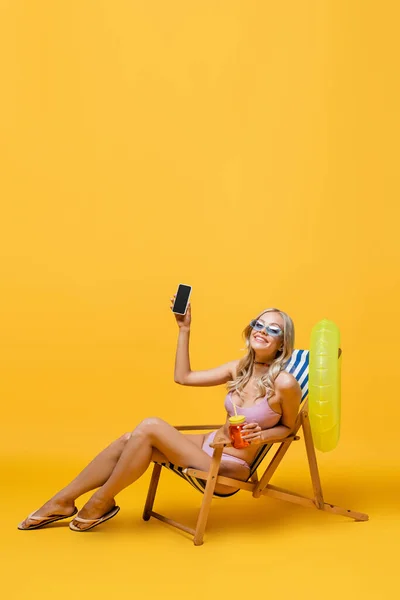 Smiling Woman Sunglasses Swimsuit Sitting Deck Chair Cocktail Smartphone Yellow — Stock Photo, Image