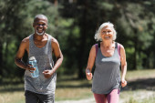 Veselý mezirasový pár se sportovní láhev jogging a při pohledu na kameru venku 
